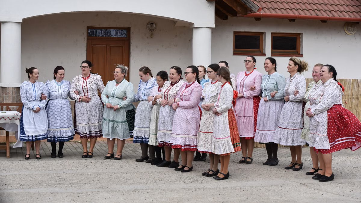Women in colorful traditional folk dresses gather outdoors, showcasing cultural attire and community celebration.